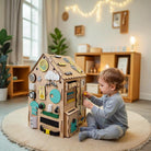 Child toddler playing with a busy board house in a cozy room.